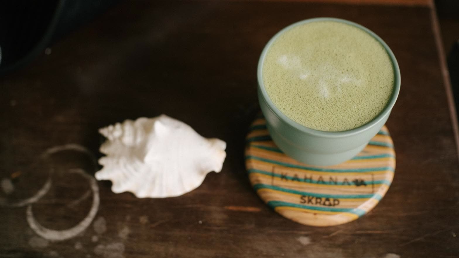 A matcha latte on a striped Kahana coaster beside a white seashell