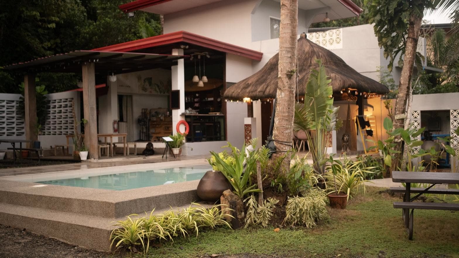 A small resort pool beside a thatched bar and tropical garden